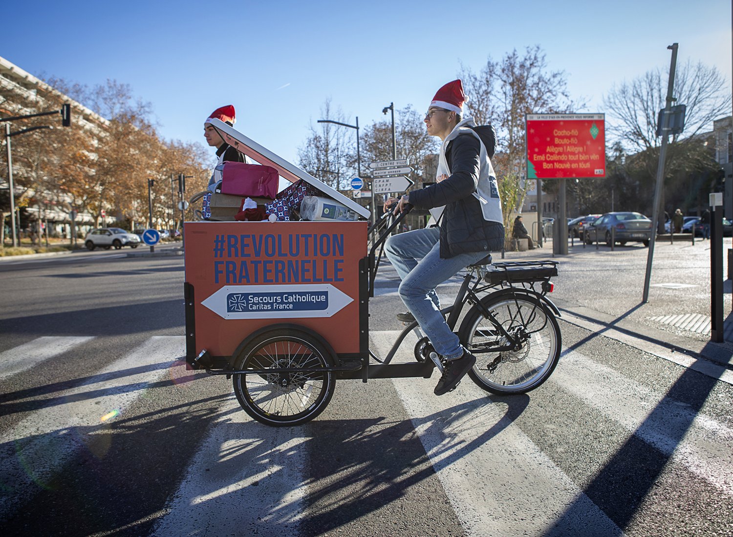 un tripoteur aux couleurs du Secours Catholique traversant une rue